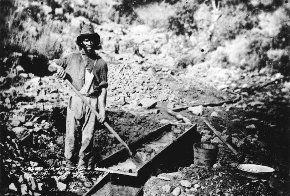 View of African American gold miner holding a shovel at sluice box.v