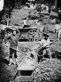 iew of 4 men, two miners at work on a long tom (one man is an African American), one man in a wagon, one man standing behind the wagon.