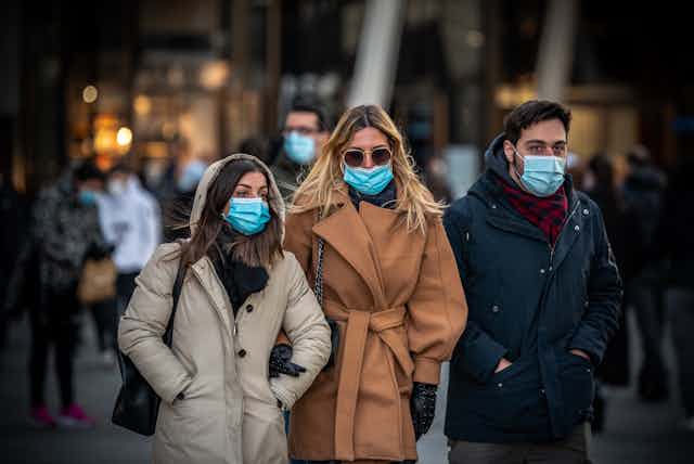 A group of friends, two women, one man, all wearing masks are out for a walk