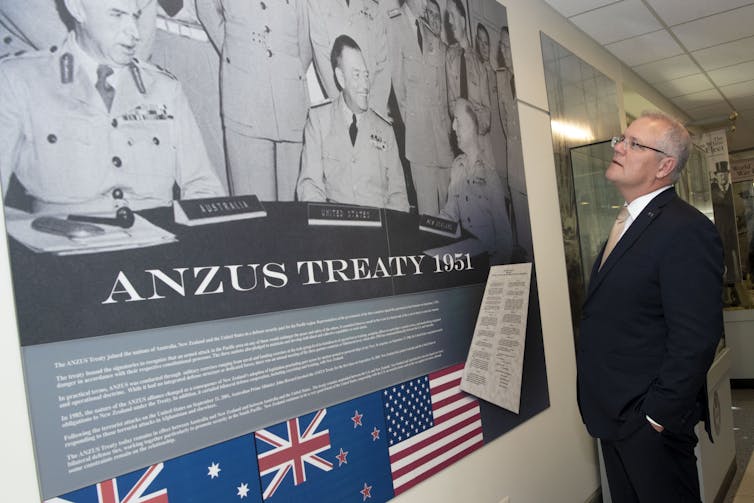 A man in a suit looks at a poster on a wall.