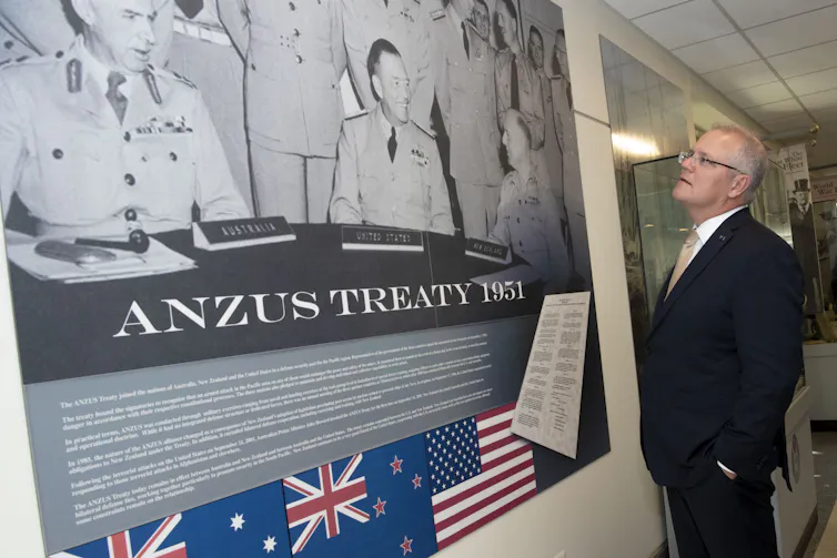 A man in a suit looks at a poster on a wall.