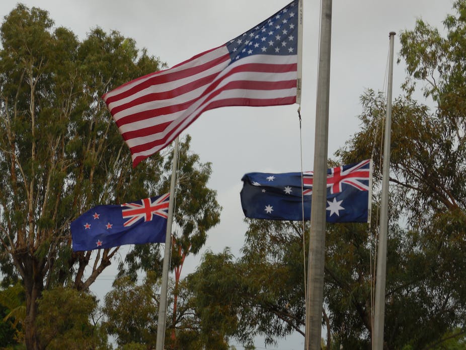 The flags of the U.S., Australia and New Zealand fly from three flagpoles