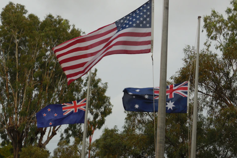 The flags of the U.S., Australia and New Zealand fly from three flagpoles