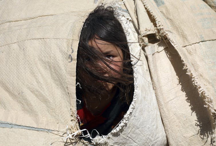 An Afghan girl peers from a tent flap, her hair obscuring her face.