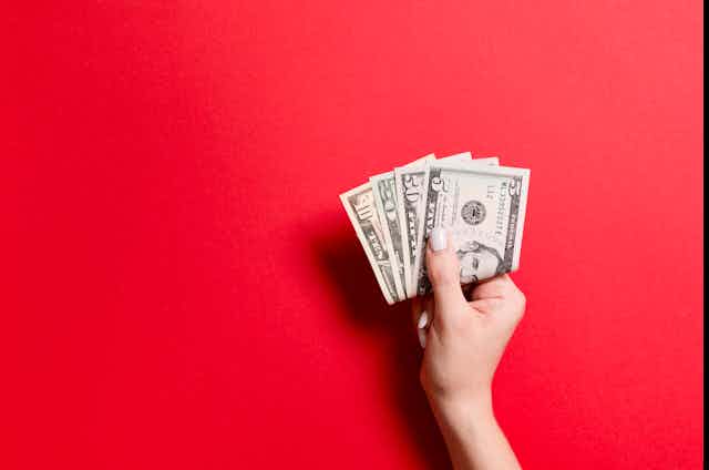 A woman's hand holding U.S. currency on a red background