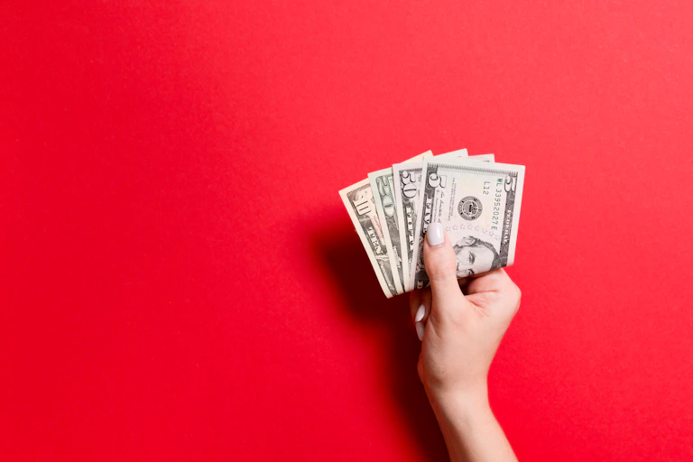 A woman's hand holding U.S. currency on a red background