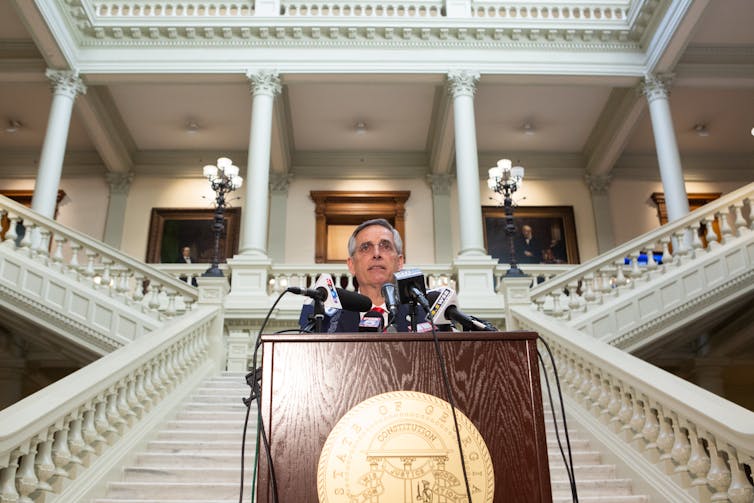 sectary of state behind a lectern and microphones