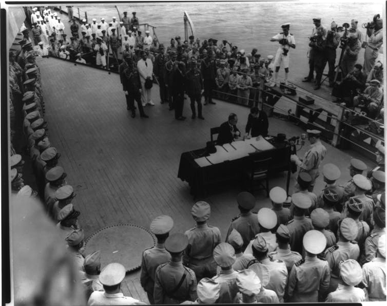 A black and white image of officials signing a document aboard a warship