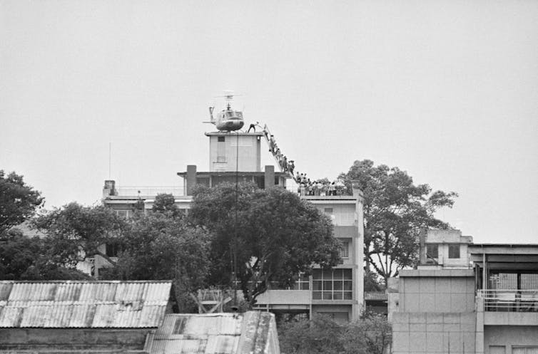 A view of a line of people climbing to a rooftop where a helicopter waits