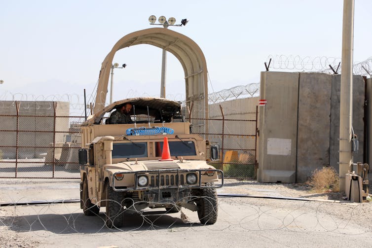 A military vehicle sits between a fence and a roll of barbed wire