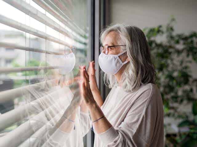 Senior woman wearing mask looks out of window