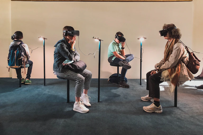 Four people sit on stools in a museum room wearing virtual reality goggles