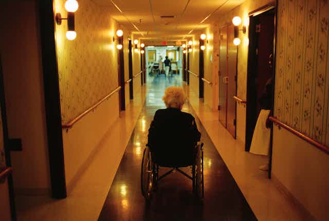 Older adult sitting in wheelchair going down the hallway of an assisted care facility. 