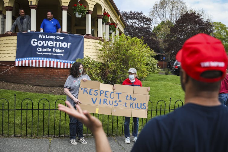 two masked people hold homemade sign that reads 'Respect the virus, it kills'