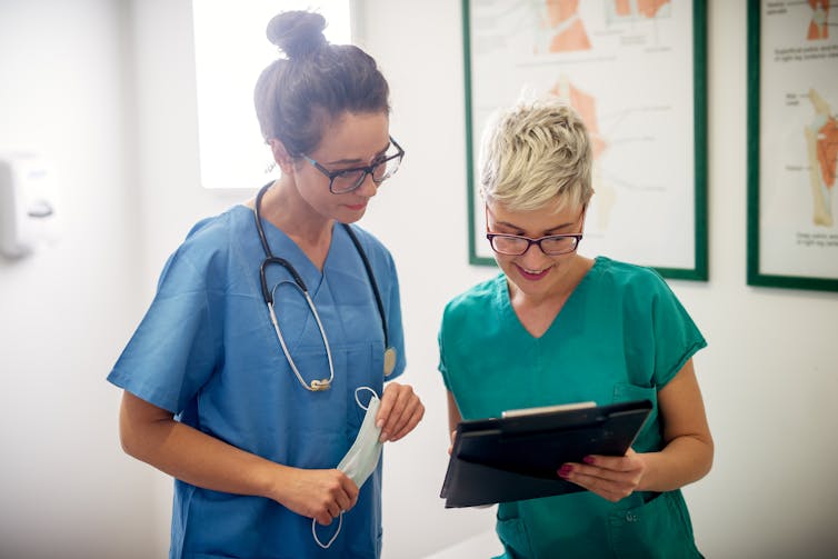 A nurse shows a doctor a patient file.