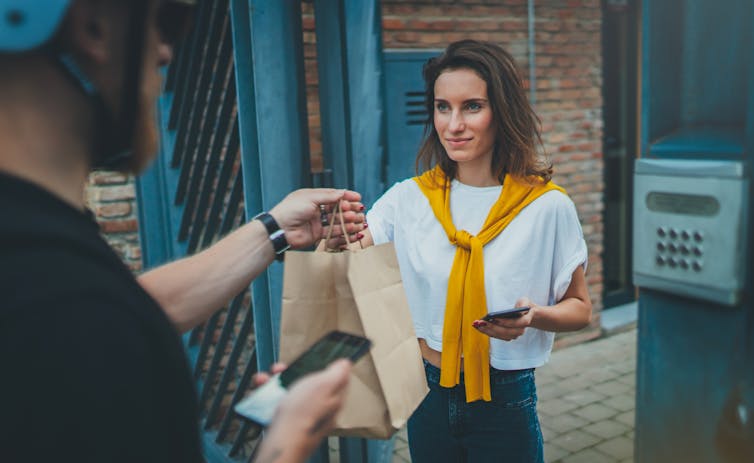 A delivery man hands a paper bag to a woman at a front gate.