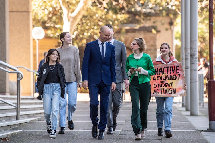 Four teenagers walk with their lawyer down a street