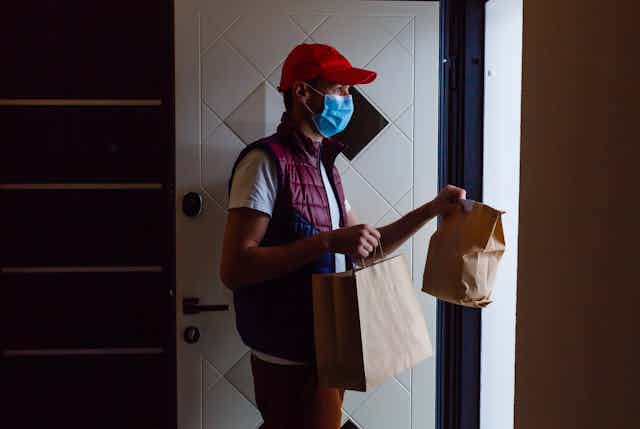 A person with food packages stands at a door.