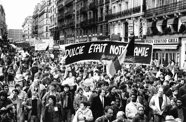 Black and white news image of a large protest in the streets of Paris, banners held aloft.