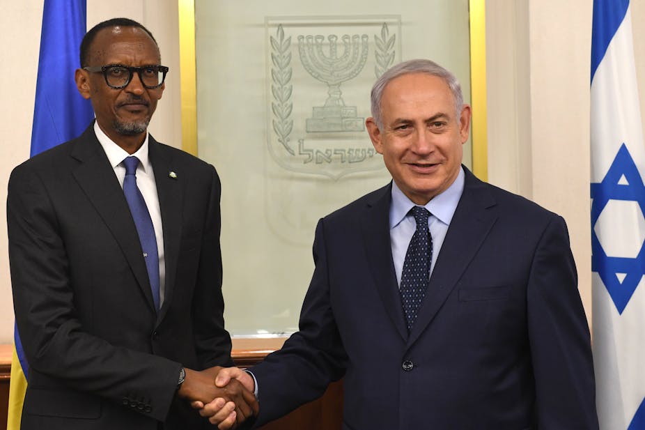 Two men shaking hands with the blue and white flag of Israel behind them.