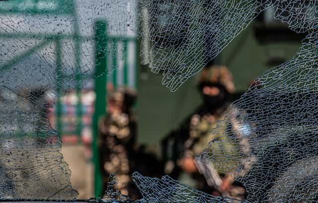 ndian government forces are seen through a broken glass of a vehicle 
