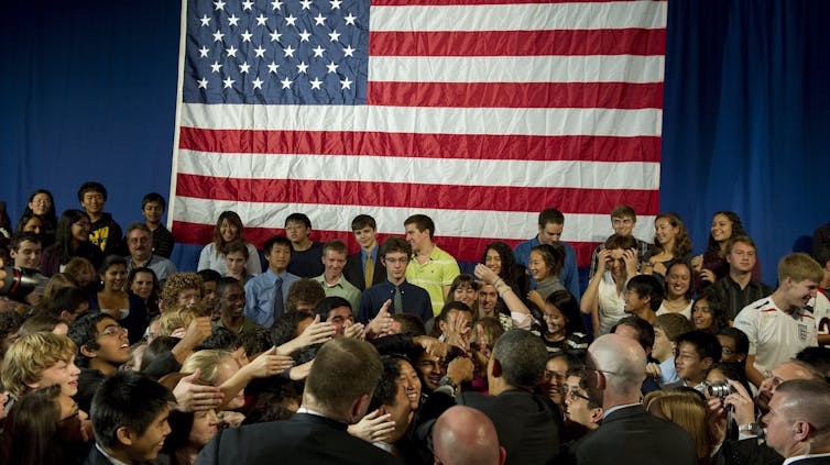 President Barack Obama shakes hands with students with large US flag in backdrop