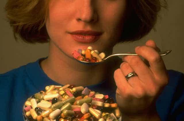 A woman eats a spoonful of pills.