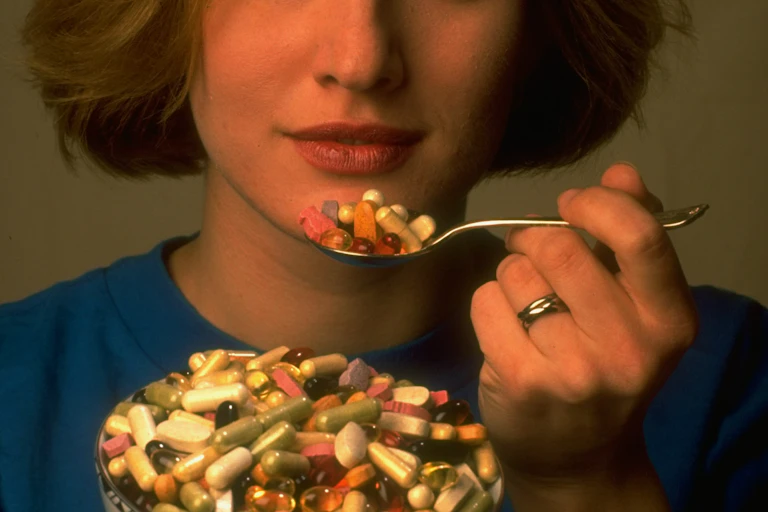 A woman eats a spoonful of pills.