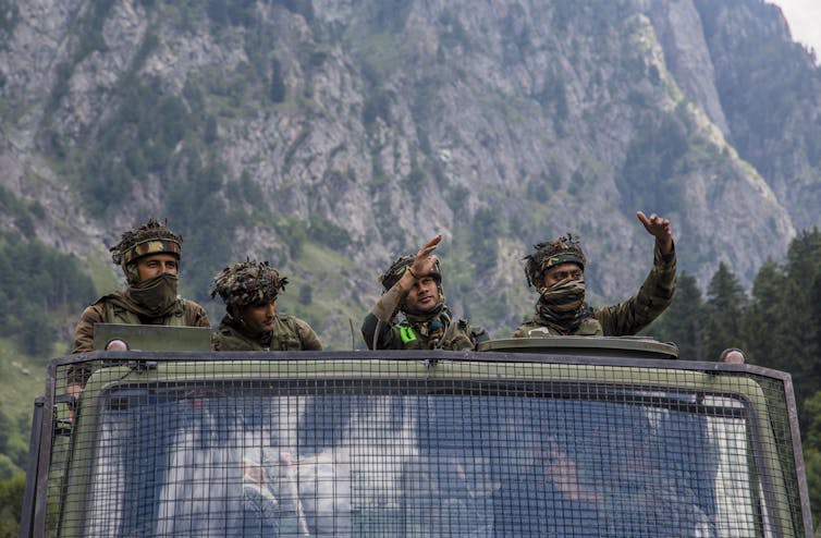 Soldiers stand in a military truck with big mountains in the background