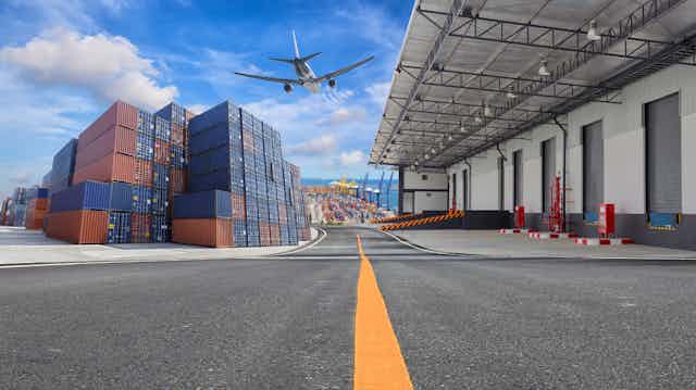 A plane flies over a loading dock and container stacks