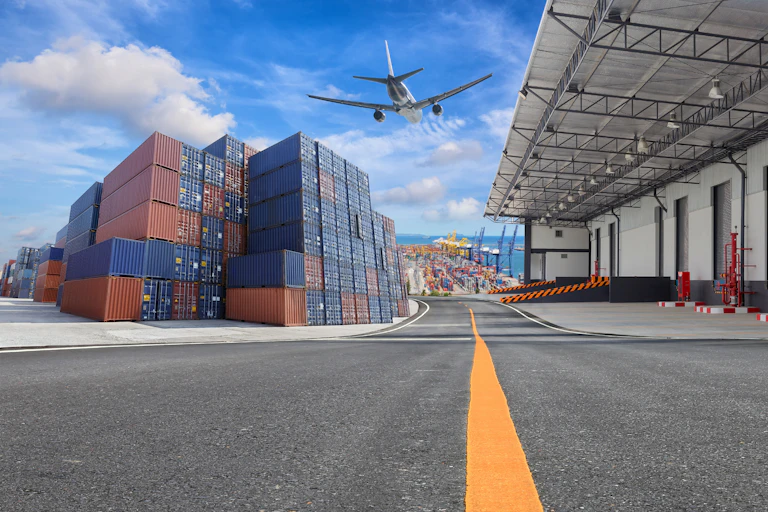 A plane flies over a loading dock and container stacks
