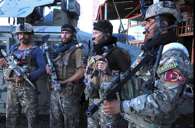 Four men in camouflage outfits stand holding rifles