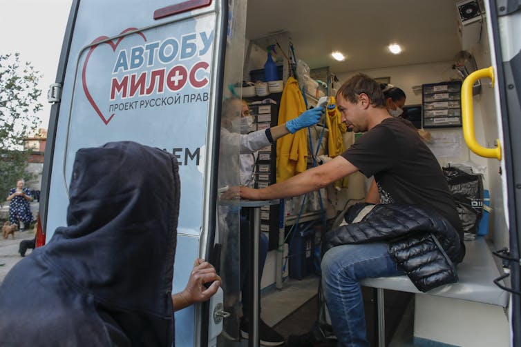 A Russian mobile vaccine station is shown, inside the station a woman checks a mans temperature