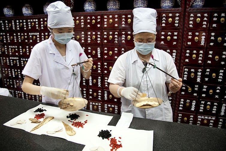 Two traditional Chinese medicine practitioners weigh and wrap herbs at Tong Ren Tang.