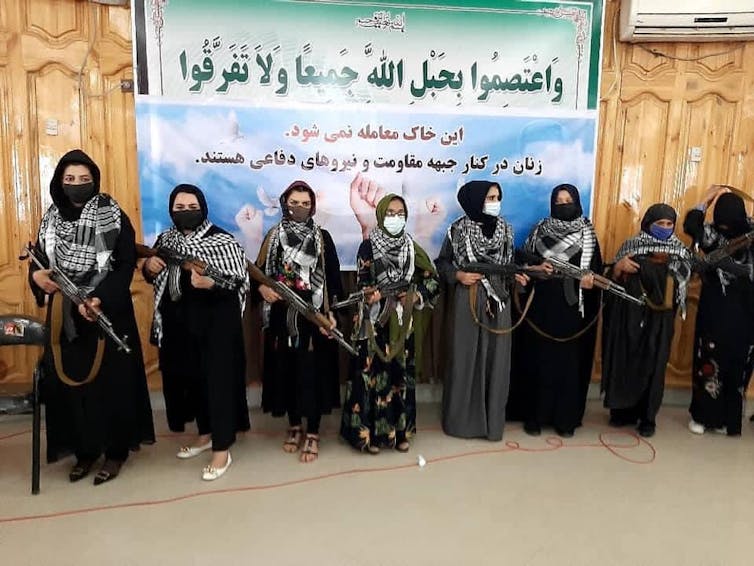 A group of women carry rifles in front of a poster