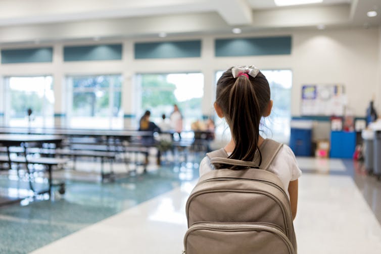 Vista traseira de uma jovem com uma mochila entrando no refeitório de uma escola