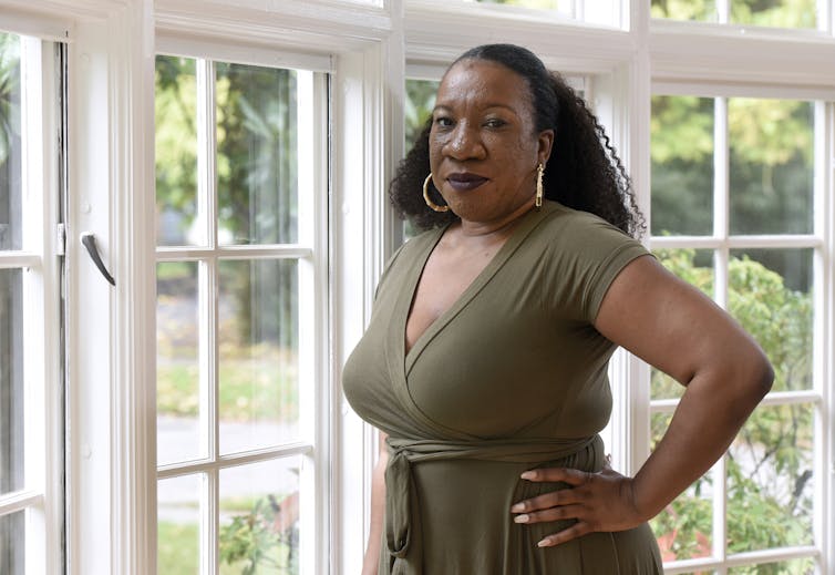 Tarana Burke stands near a window with her hands resting on her hips.