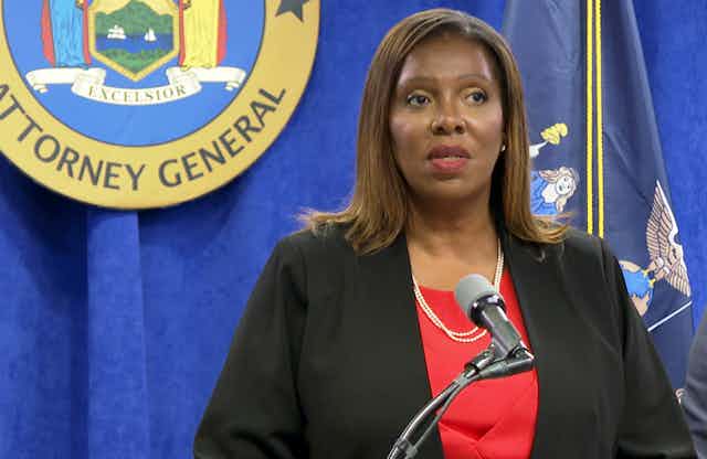 Letitia James stands in front of a microphone with the attorney general seal on a blue curtain behind her during a press conference