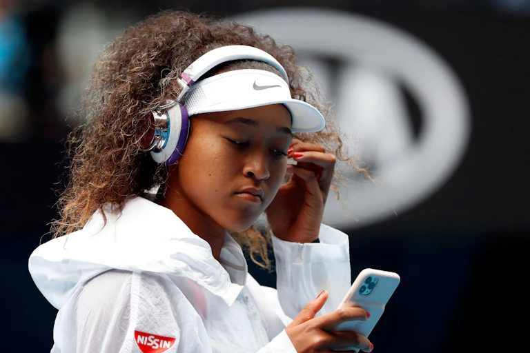 Naomi Osaka wears headphones and looks at phone.
