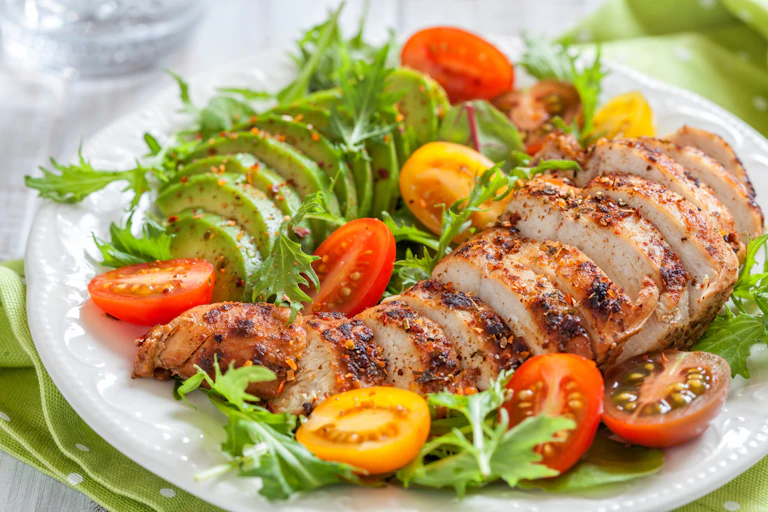 A salad with sliced tomatoes, chicken breast, and avocados.