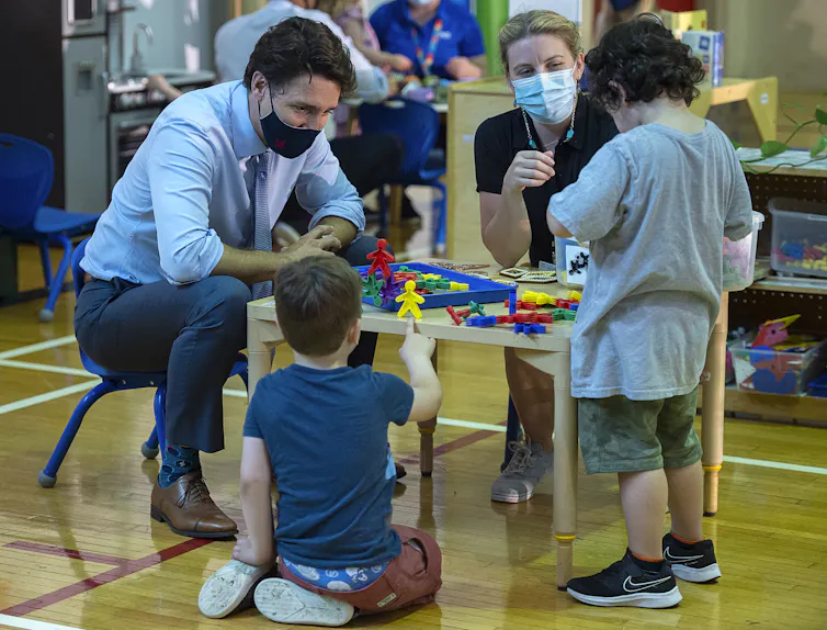 Justin Trudeau, wearing a mask, sits at a table playing games with children.