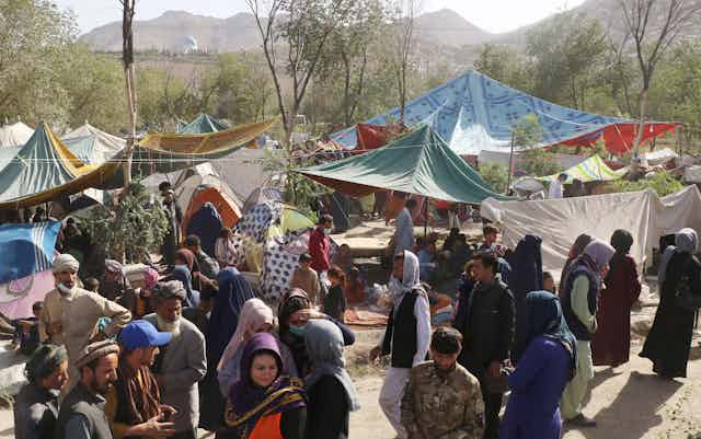 A crowd of people gathers in an open space partially covered by makeshift tents and canopies.