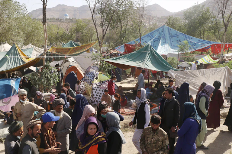 A crowd of people gathers in an open space partially covered by makeshift tents and canopies.