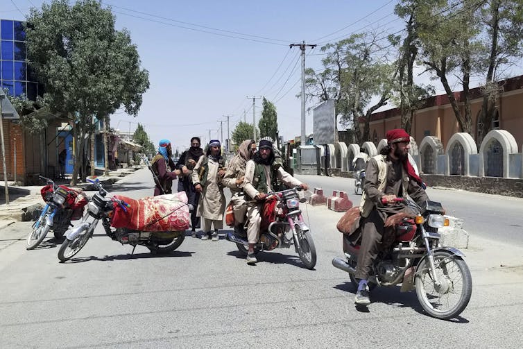 Armed men on motorcycles ride down a street