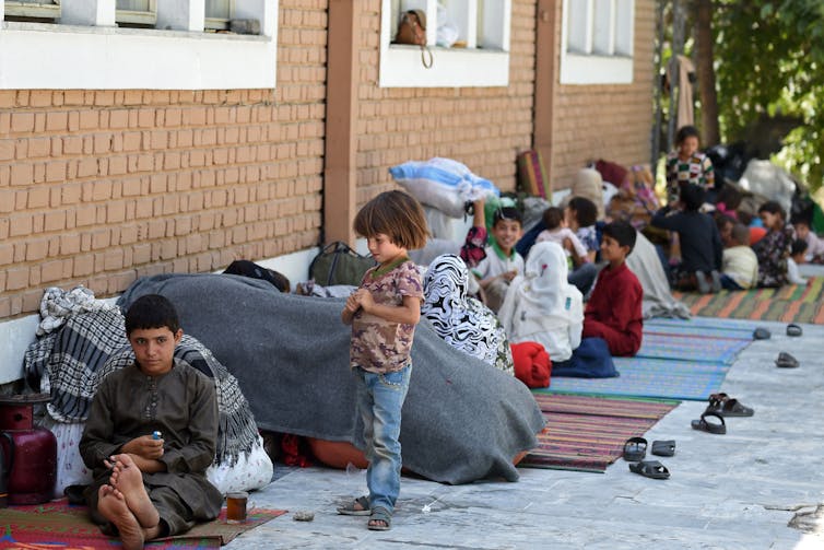 Children sit on carpets outside a brick building