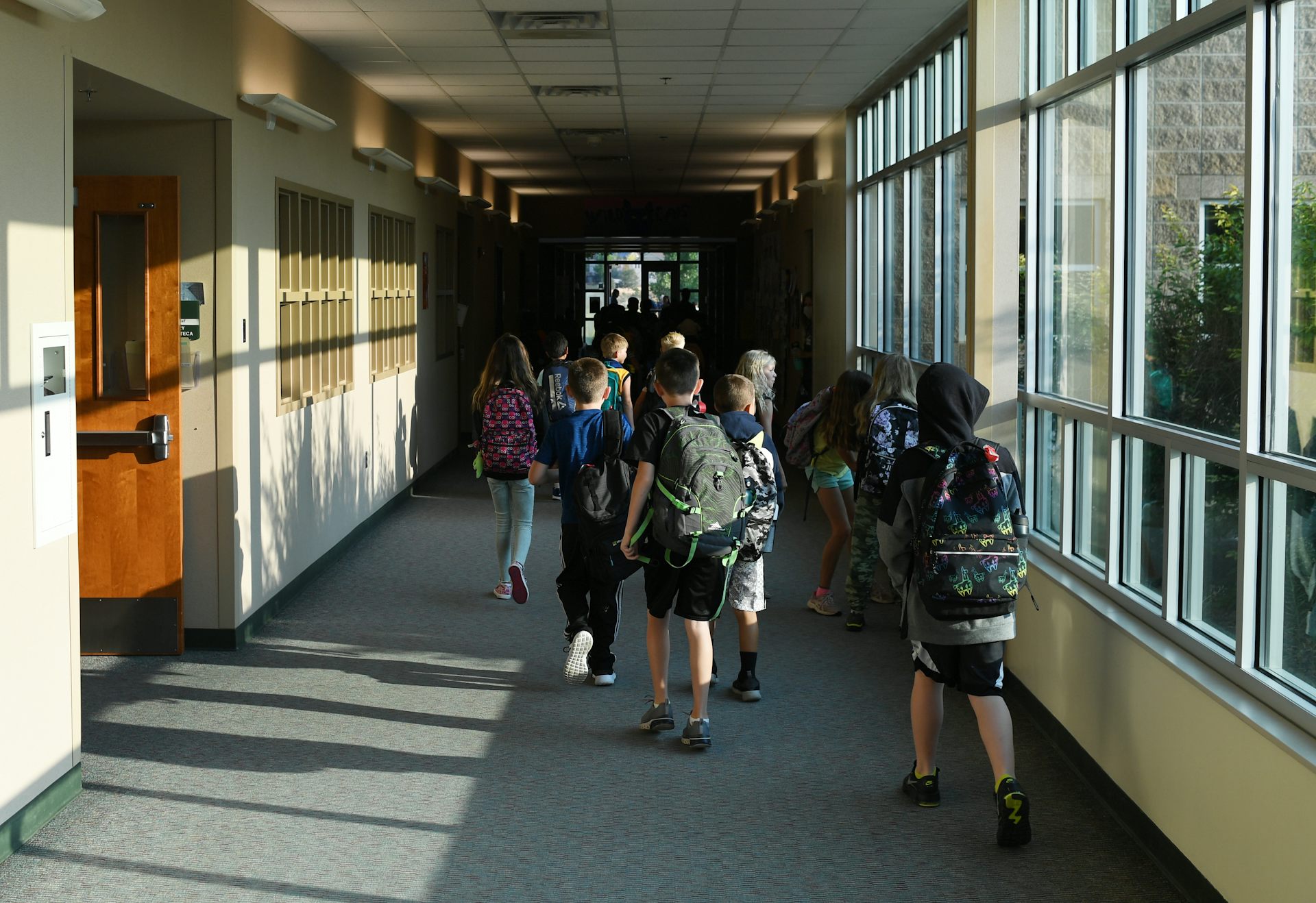 Students wearing backpacks walk down school corridor
