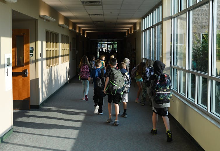 Students wearing backpacks walk down school corridor