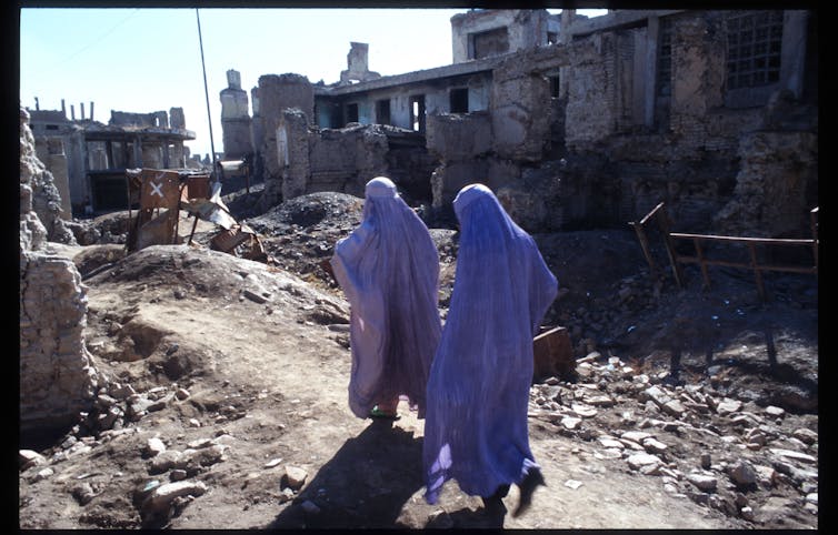 Women in purple burqas walk amid a ruined city street