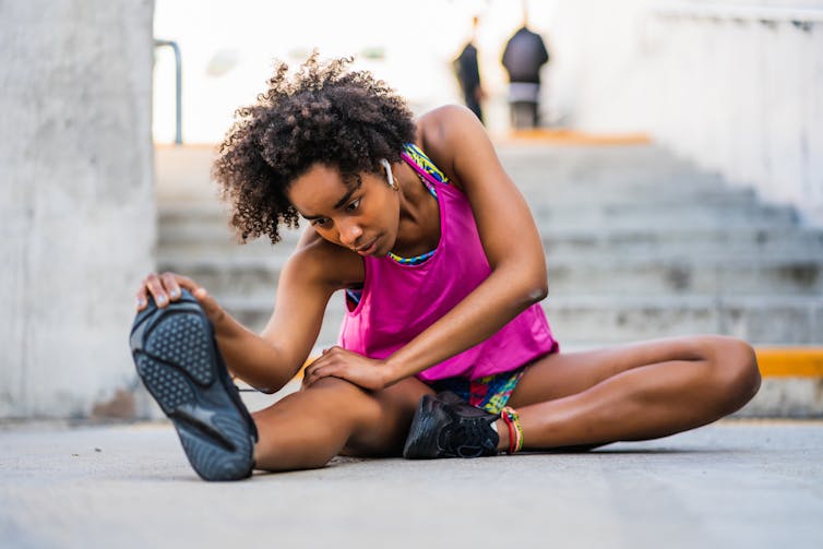 Jeune femme en tenue de sport pratiquant des étirements assise sur le sol, au pied d’un escalier.
