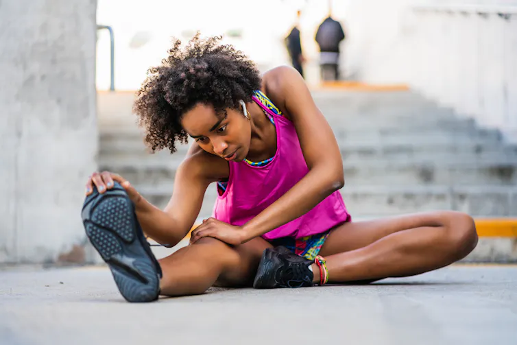 Jeune femme en tenue de sport pratiquant des étirements assise sur le sol, au pied d’un escalier.